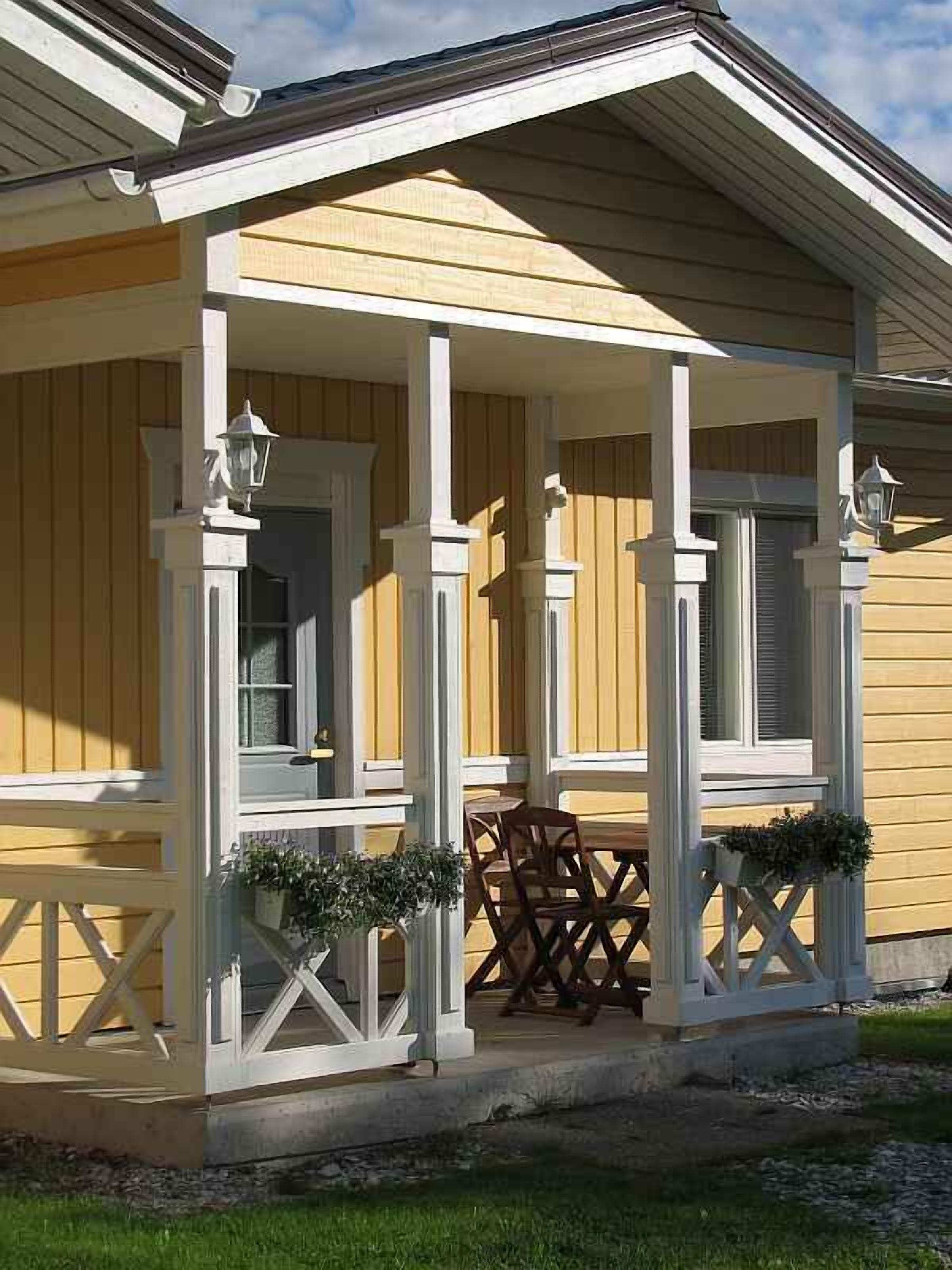Een overdekt terras met witte leuningen en zuilen, een houten tafel en stoelen.