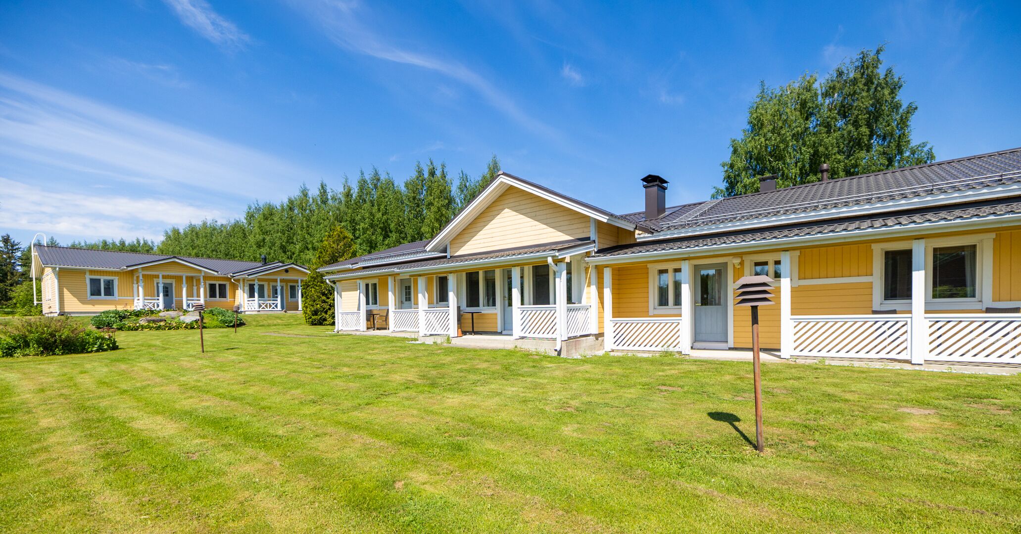 Rivi keltaisia mökkejä, joissa on valkoiset kaiteet, ja jokaisessa on kuisti ja savupiippu.