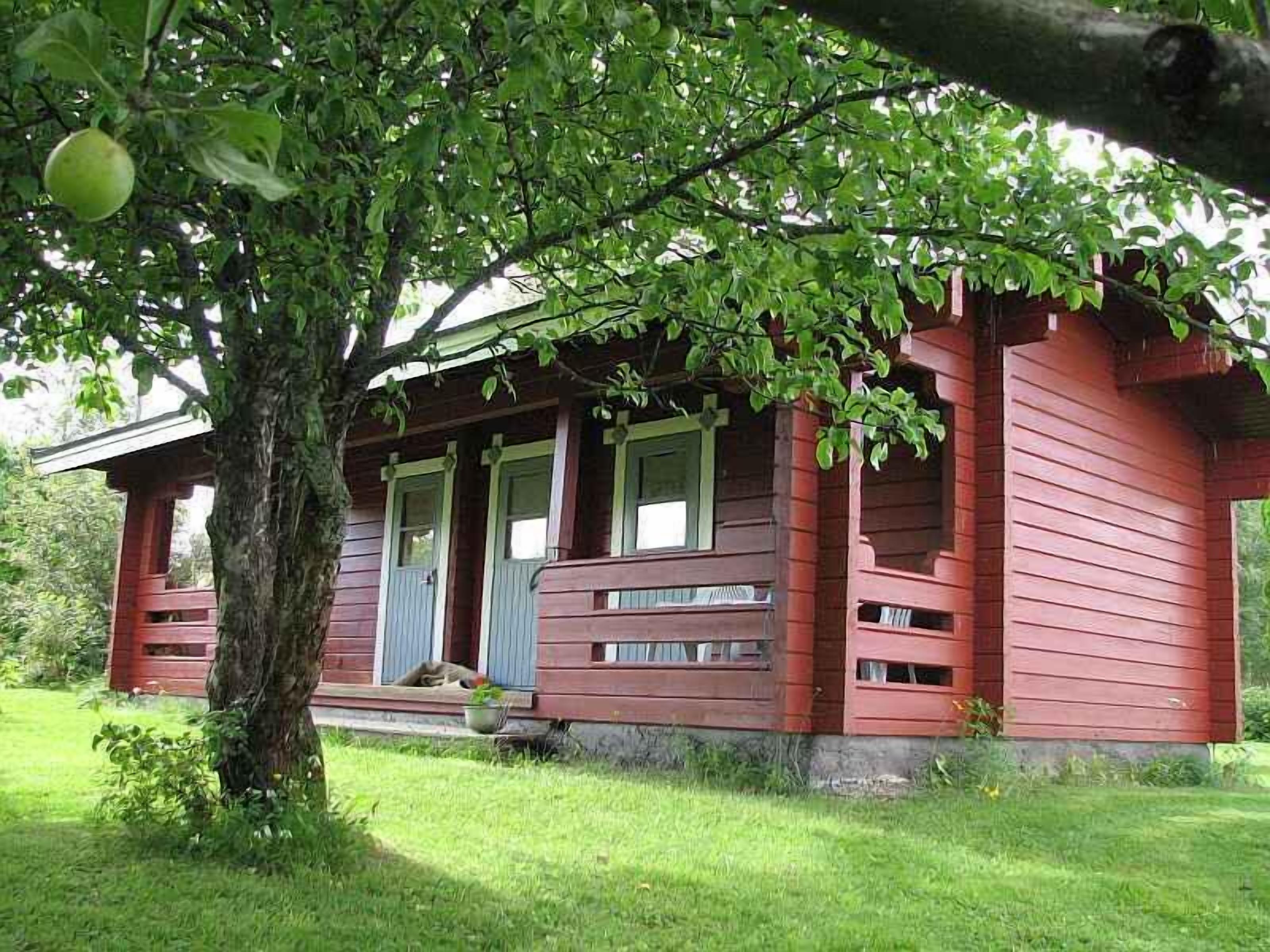 Ein rotes Holzhaus mit Veranda, umgeben von viel Grün.