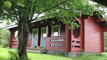 Ein rotes Holzhaus mit Veranda, umgeben von viel Grün.