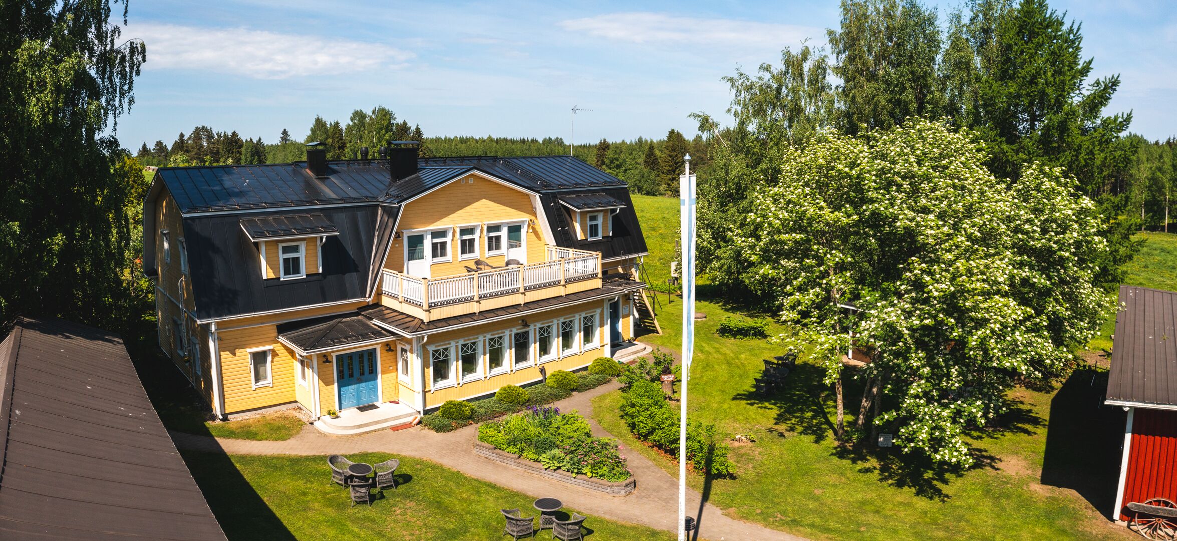Ein zweistöckiges Haus mit Balkon, umgeben von einem gepflegten Garten und einem großen Baum.