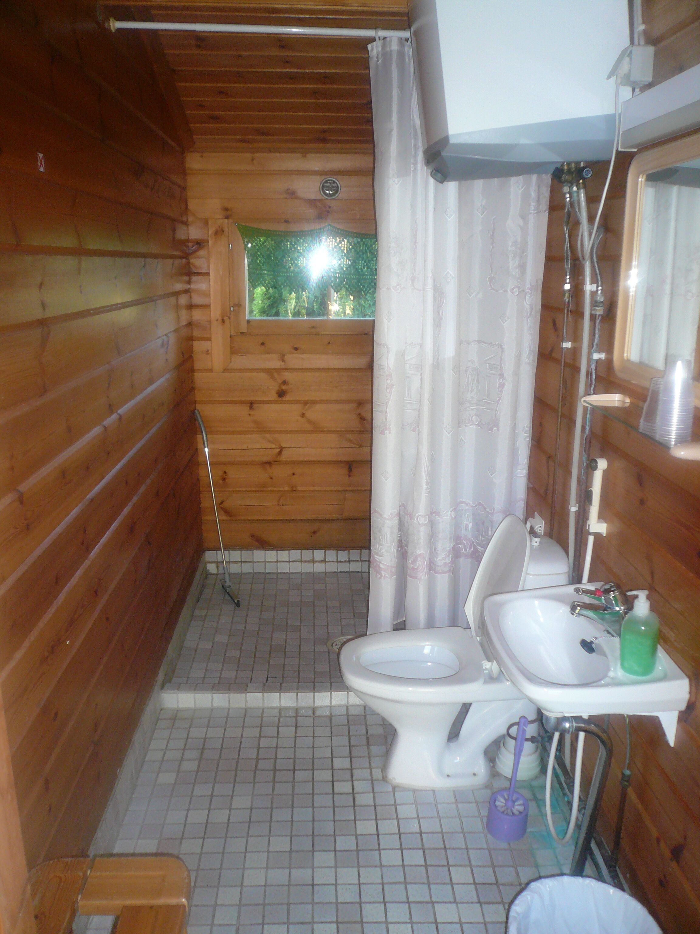 A small, wooden cabin bathroom with a toilet, sink, and shower.