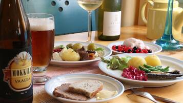 Una mesa con platos de comida, una botella de cerveza Mokkila Vaalea, una copa de vino blanco y una botella de vino Leyla.