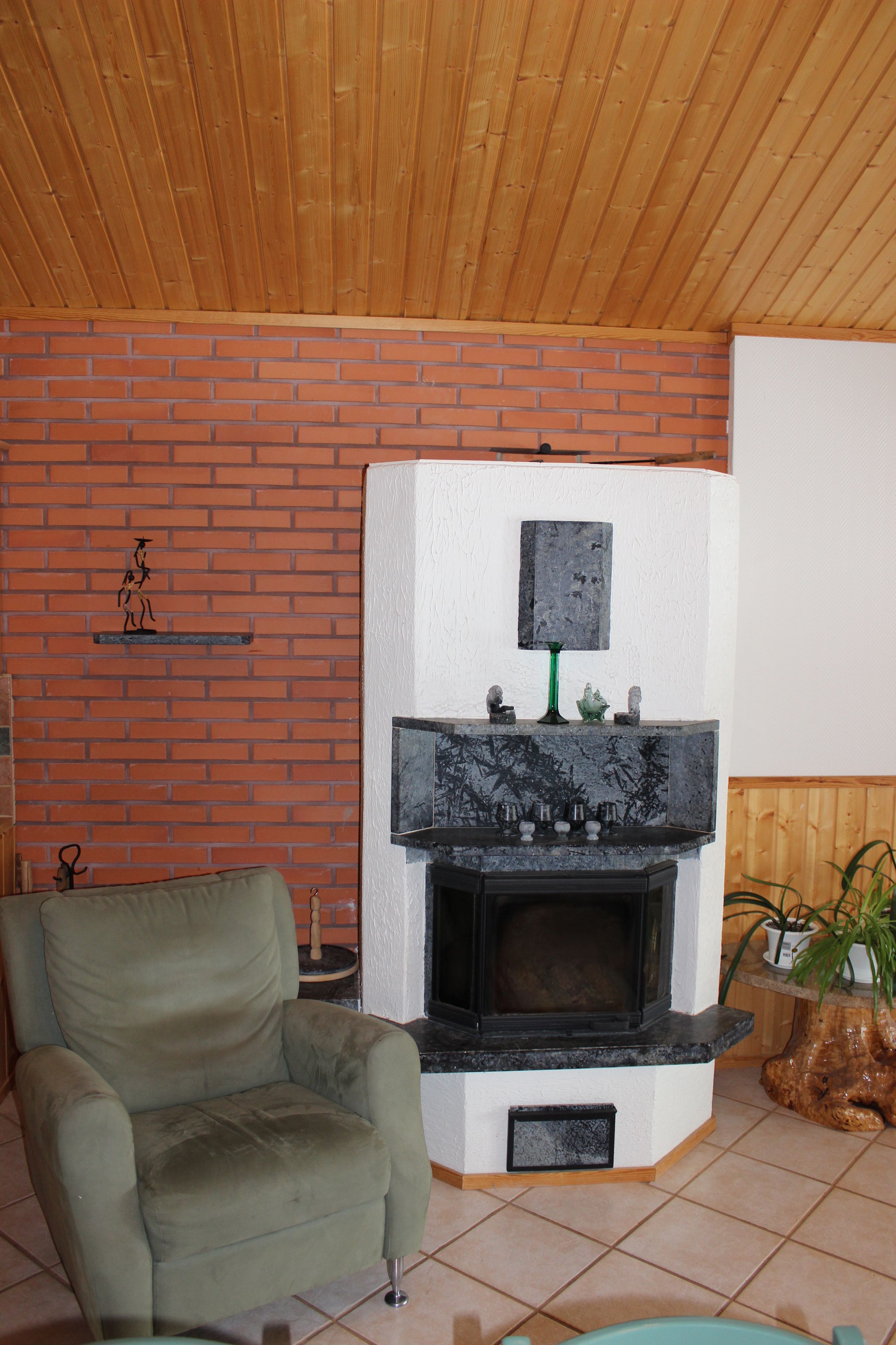 A room with a brick wall, a fireplace, a green armchair, and a wooden ceiling.
