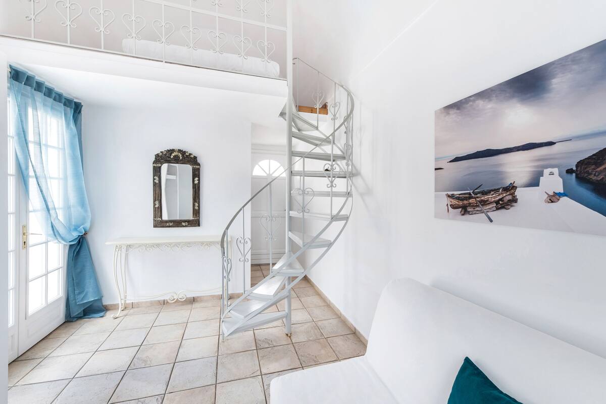A modern interior with a spiral staircase, a white console table, a mirror, and a painting of a coastal scene.