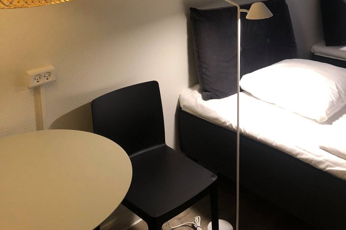 Une chambre d’hôtel avec un lit, un bureau, une chaise et une lampe suspendue.