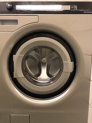 Vue de face d’un lave-linge à chargement frontal de qualité professionnelle, avec un panneau de commande situé au-dessus de la porte.