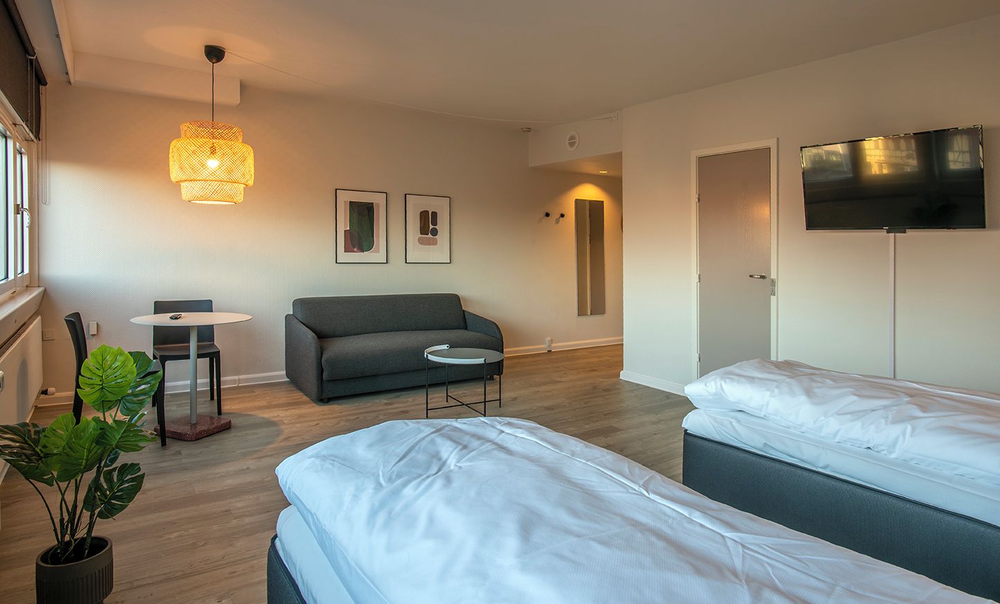 Ein modernes Hotelzimmer mit zwei Betten, einer Couch, einem kleinen runden Tisch und einem an der Wand befestigten Fernseher.