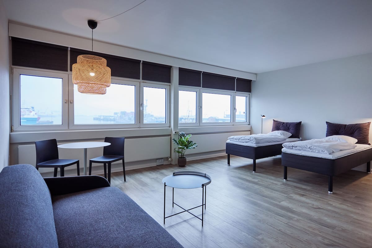 Une chambre d’hôtel moderne avec un canapé, deux lits, une petite table et de grandes fenêtres.