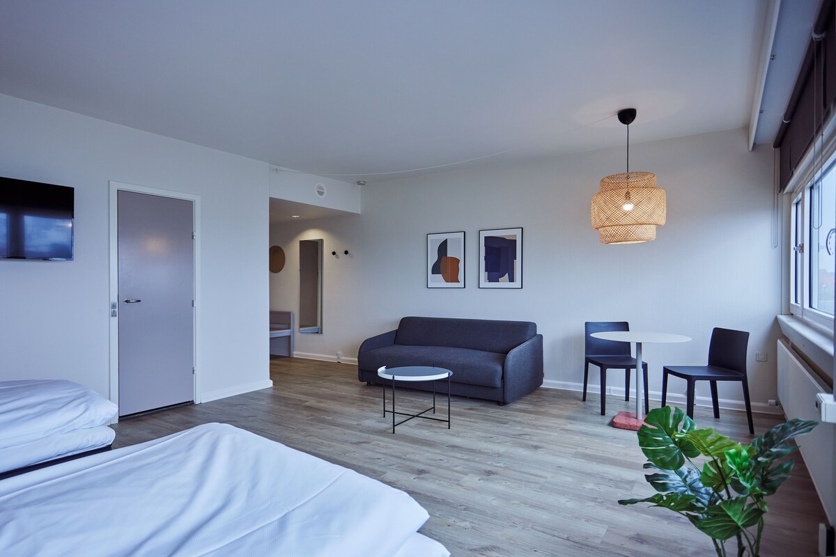 Een moderne hotelkamer met een bed, een sofa, een klein rond tafeltje en een plant in pot.