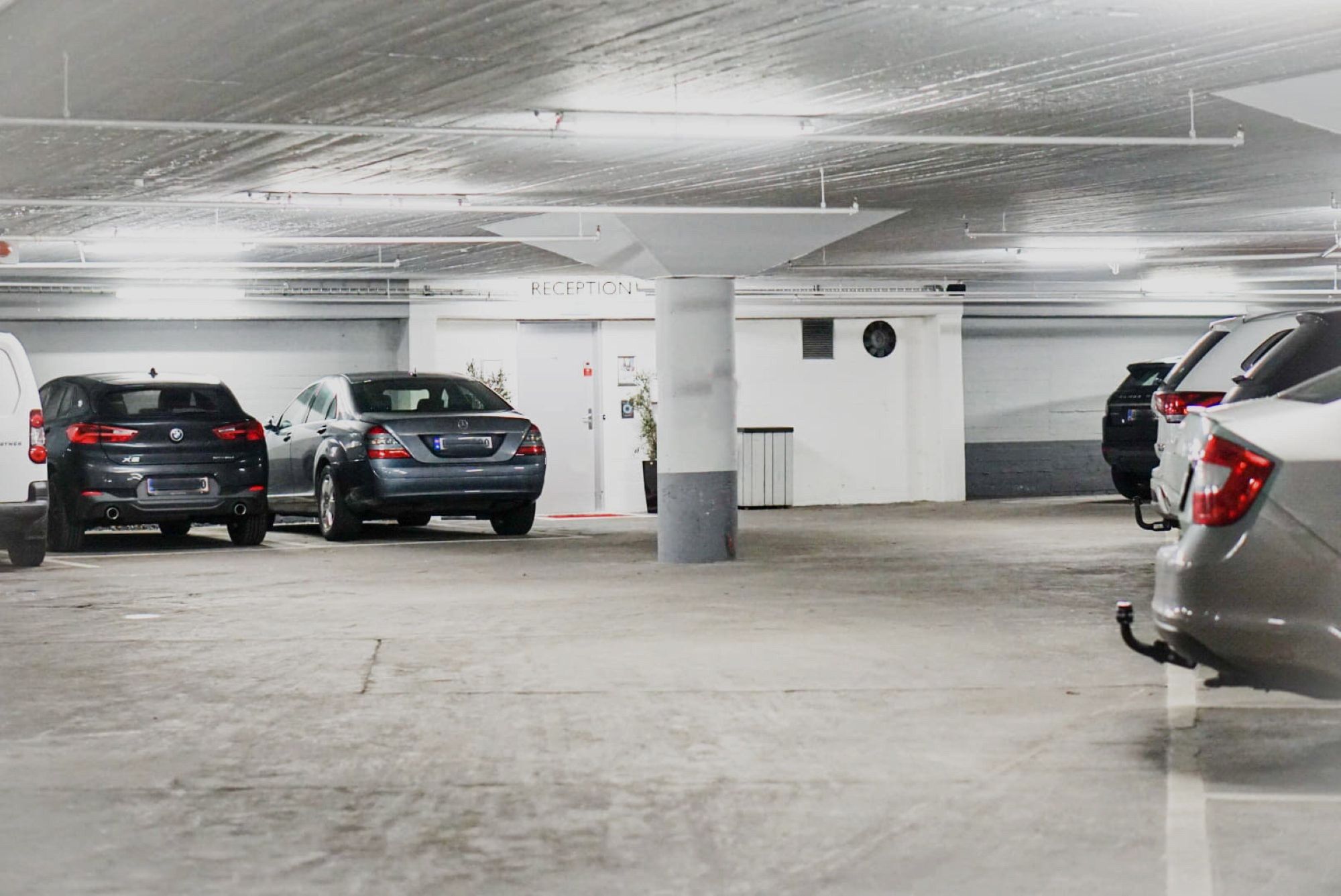 Un aparcamiento con varios coches estacionados, una zona de recepción y un pilar.