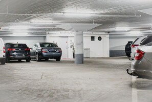 Un parking souterrain où sont garées plusieurs voitures, un espace d’accueil et un pilier.