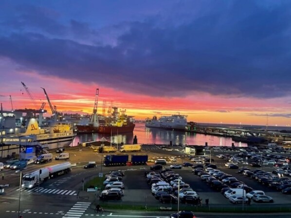 Un port où un grand navire de transport est amarré, entouré de voitures garées et de bâtiments industriels.