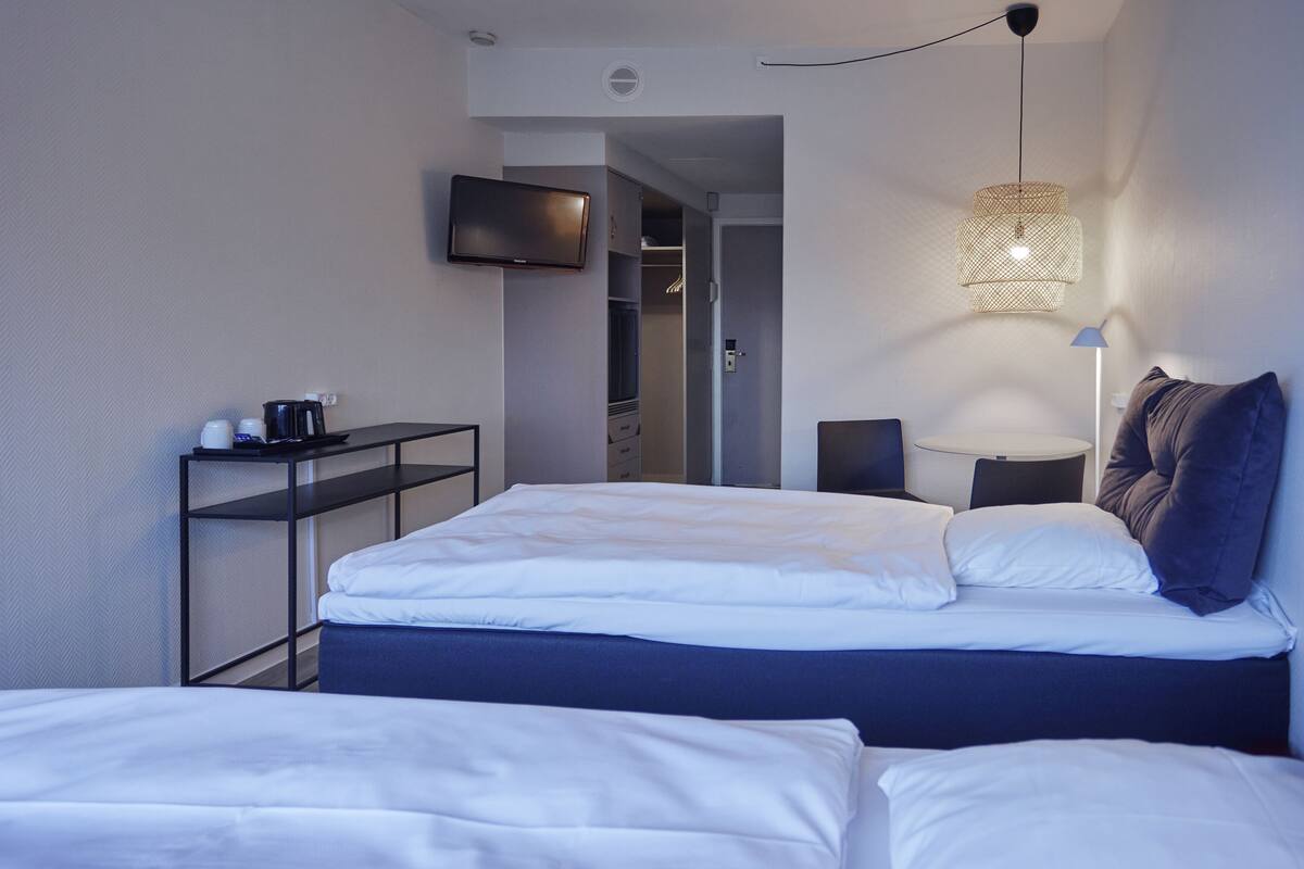 Une chambre d’hôtel moderne avec un lit bien fait, un téléviseur fixé au mur, une petite table avec une lampe et un dressing.
