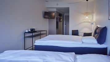 Una habitación de hotel moderna con una cama bien hecha, un televisor montado en la pared, una mesita de noche con una lámpara y un vestidor.