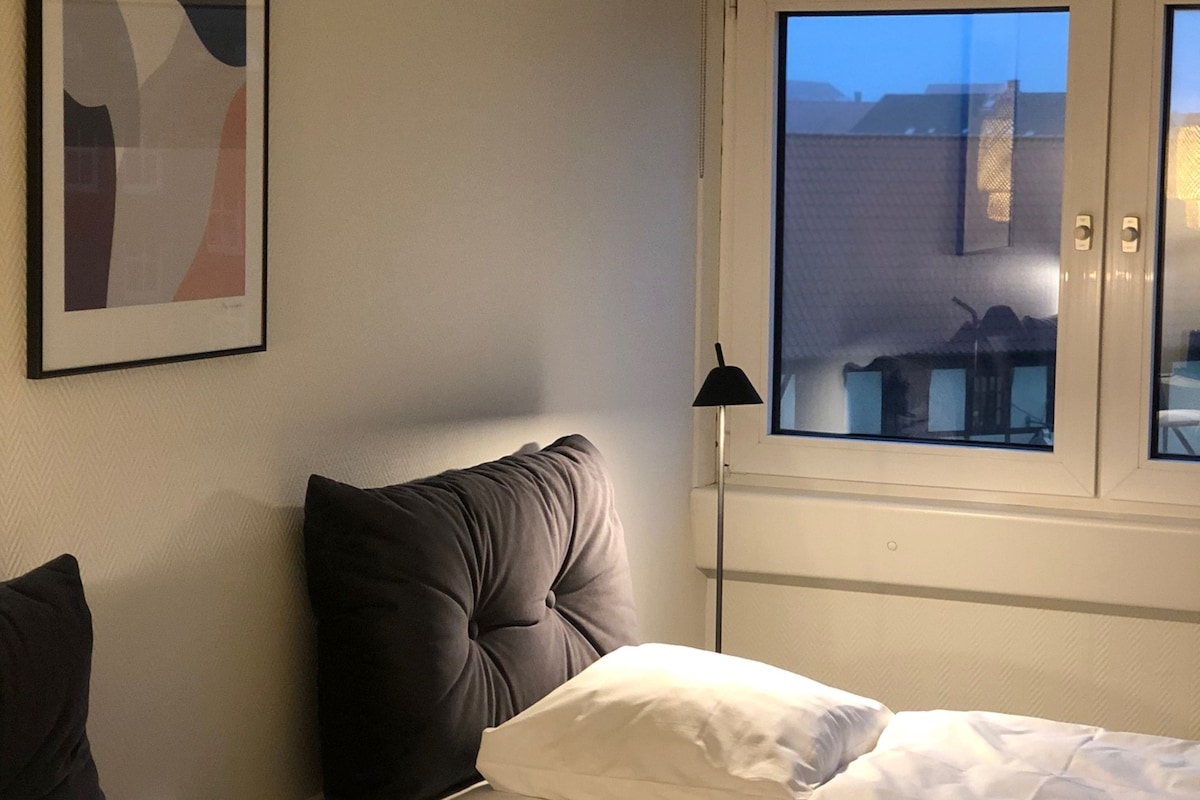 Une chambre d’hôtel avec un lit, une fenêtre donnant sur un beau paysage et une œuvre d’art abstraite encadrée accrochée au mur.