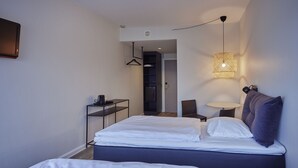 Ein modernes Hotelzimmer mit Bett, Nachttisch, Lampe und Kleiderschrank.