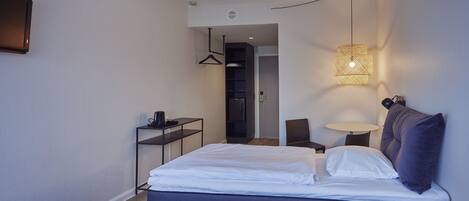 A modern hotel room with a bed, bedside table, lamp, and a wardrobe.