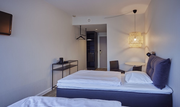 Een moderne hotelkamer met een bed, nachtkastje, lamp en een kledingkast.