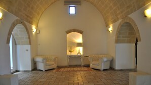 A room with a high arched ceiling, two white armchairs, a small table, and a rug on the floor.
