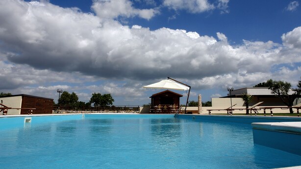 A swimming pool with a covered seating area and a building in the background.