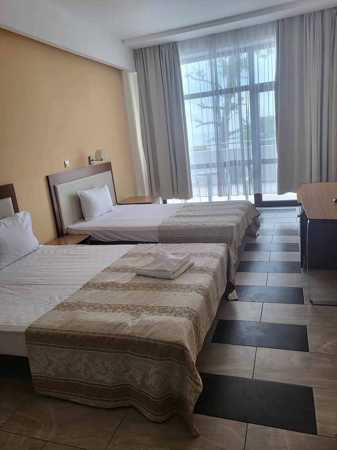 Habitación de hotel con tres camas, un escritorio y vistas al exterior.