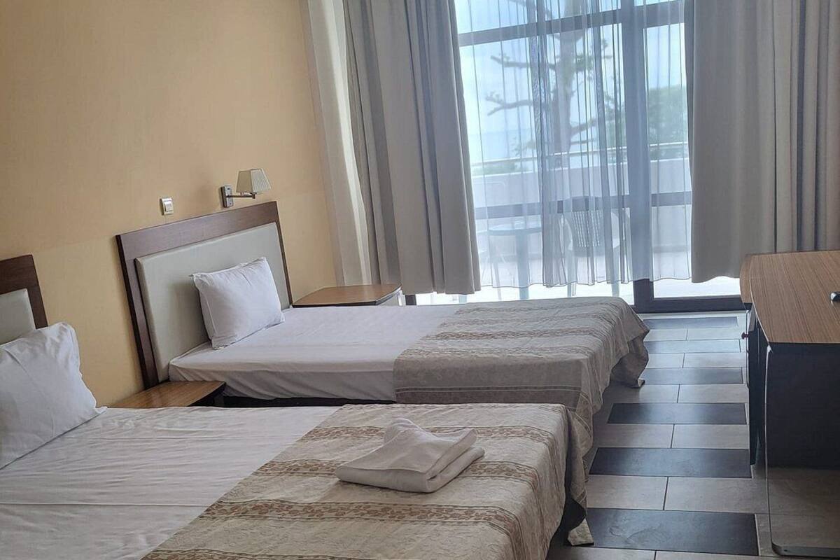 A hotel room with three beds, a desk, and a view of the outdoors.