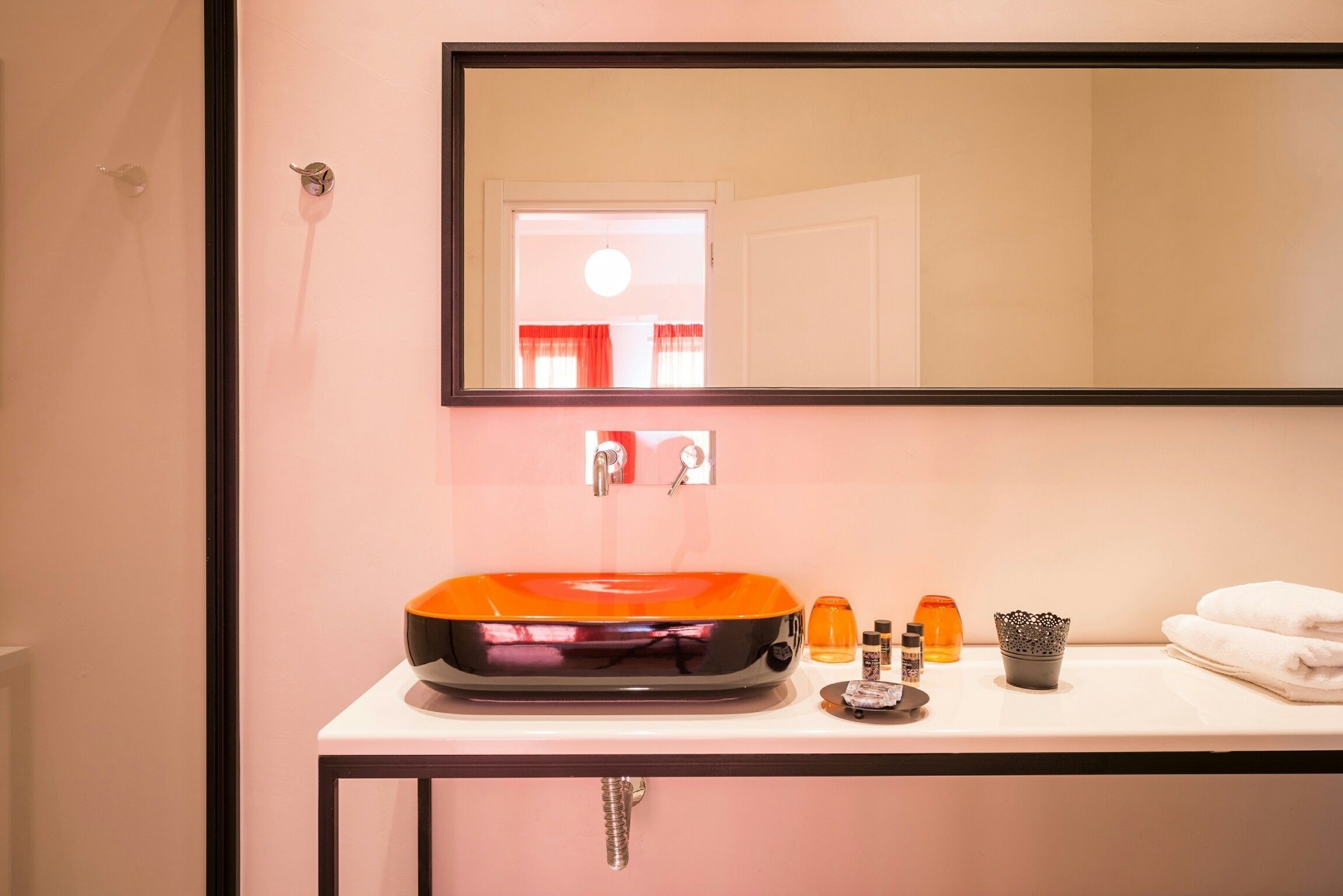 Une salle de bain avec un lavabo blanc, un miroir au-dessus et un porte-serviettes avec des serviettes pliées.