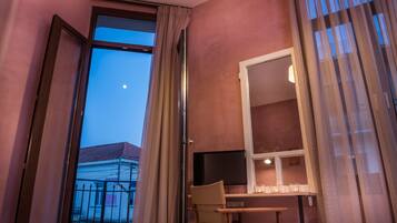 A hotel room with a balcony, a desk with a chair, a television, and a window with curtains.