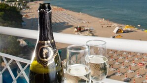 A bottle of Albena sparkling white wine and two glasses on a table with a view of a beach and ocean. - Hotel Boryana (Kranevo)