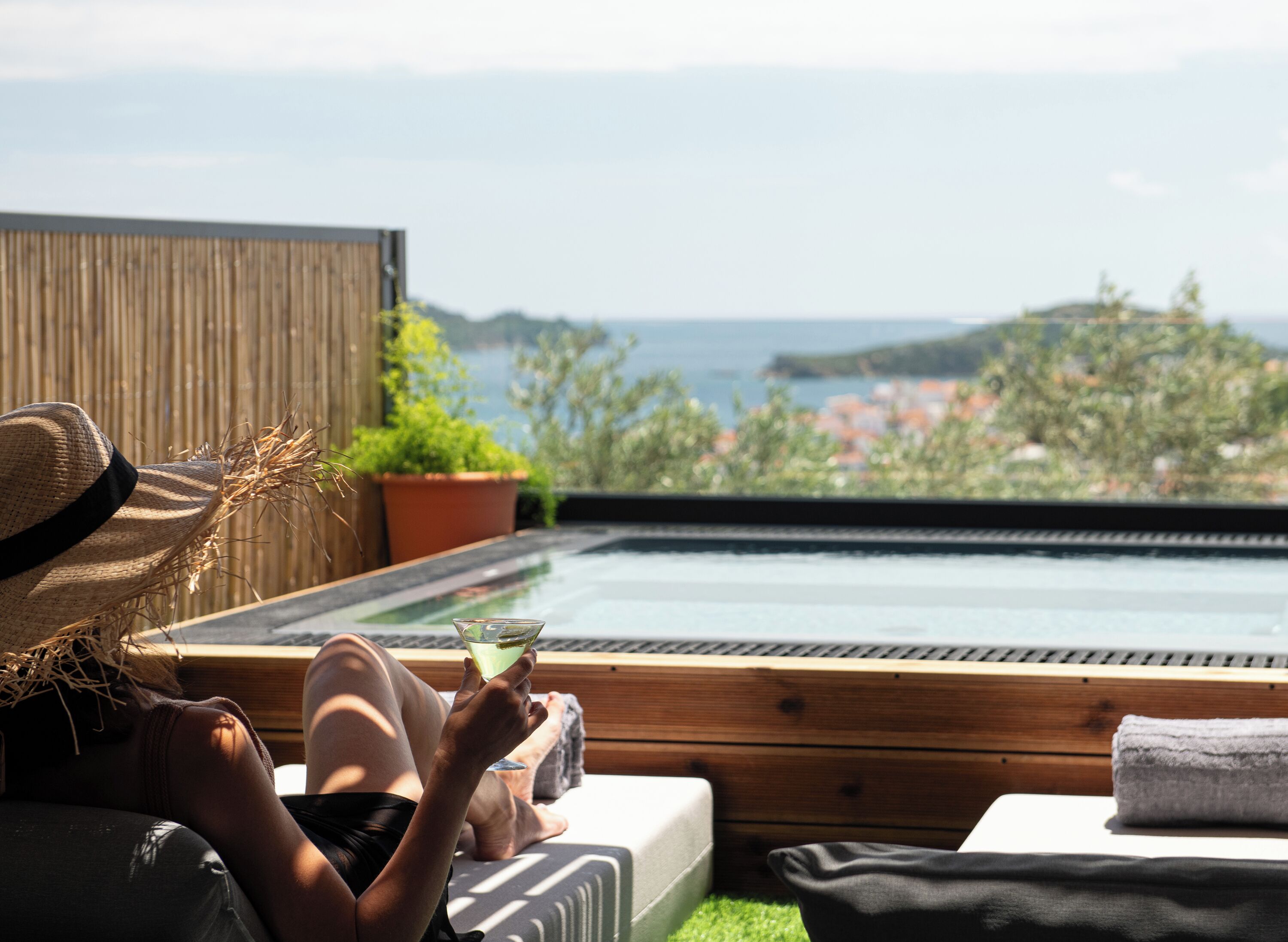 En person som kopplar av vid en pool med utsikt över havet och kullarna.