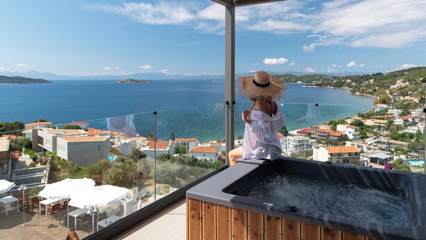 A person sitting on a balcony with a view of the sea and a town. - Poseidon Villas (Skiathos)