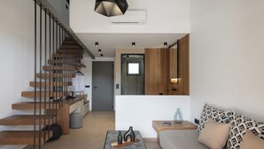 A modern living room with a staircase, a sofa with patterned cushions, a coffee table with decorative items, and a wooden cabinet. - Poseidon Villas (Skiathos)