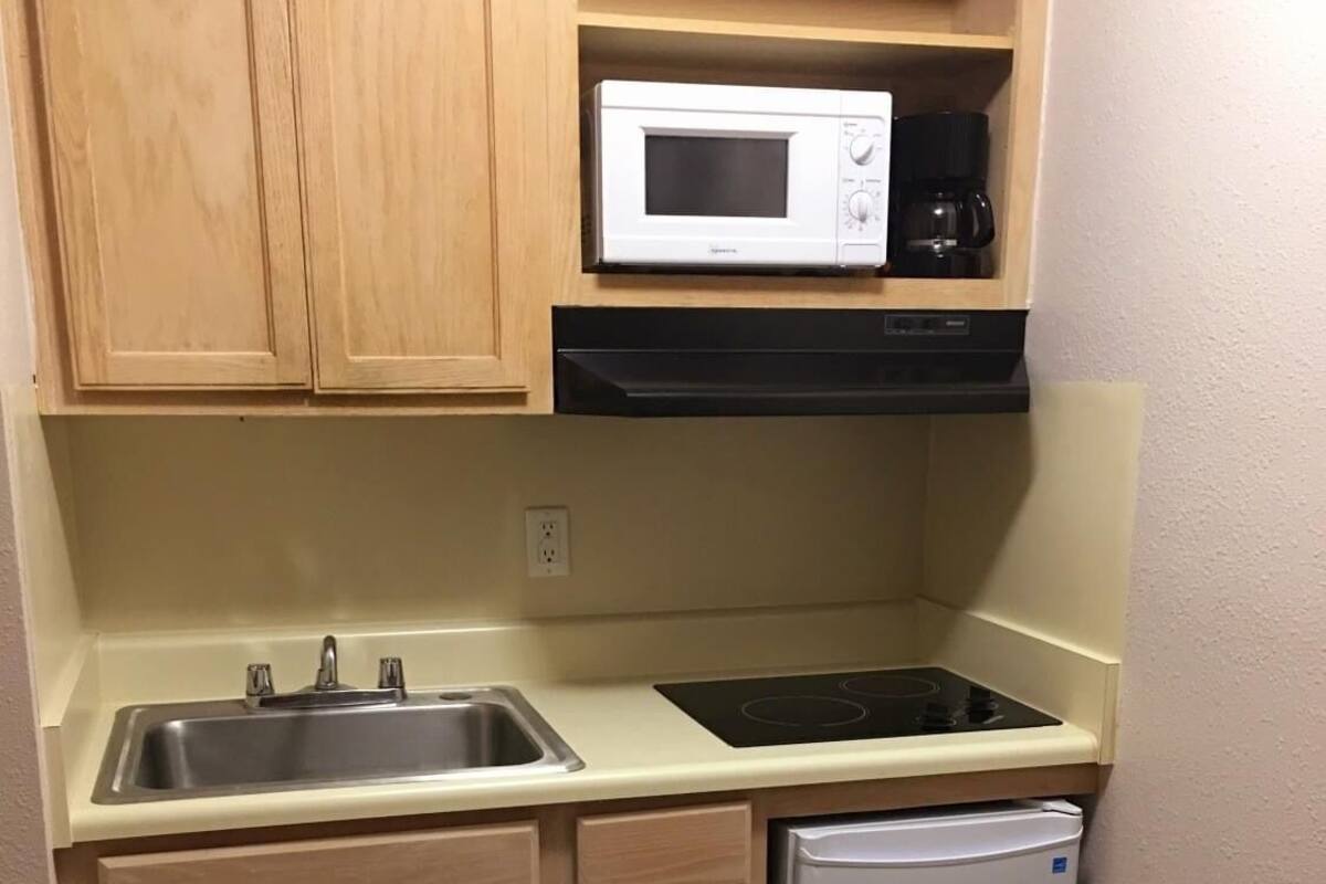 A compact kitchen with wooden cabinets, a stainless steel sink, a black stove, a white microwave, and a white refrigerator.