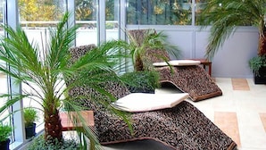 A sunlit indoor space with large windows, a seating area with patterned cushions, and various potted plants. - Hotel Flamingo (Albena)