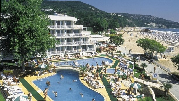 A resort with a large pool area, multiple levels of a building, and a beach in the background. - Hotel Kaliopa (Albena)