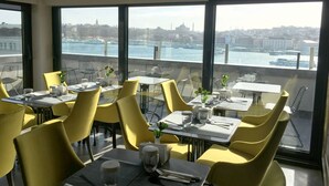 A dining area with yellow chairs and tables, large windows with a city view, and a modern interior design. - Nordstern Hotel Galata (Istanbul)