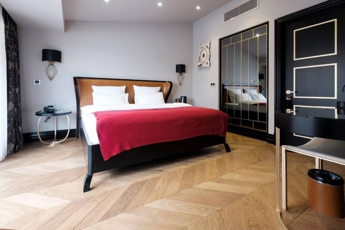 Una habitación de hotel moderna con una cama grande, una mesita redonda, un armario con espejo y un cubo de basura.