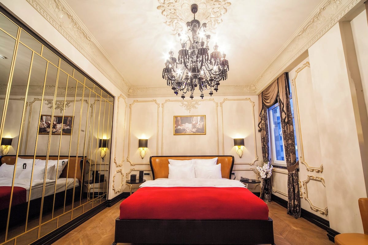 A luxurious bedroom with a large bed, ornate ceiling, and a chandelier.