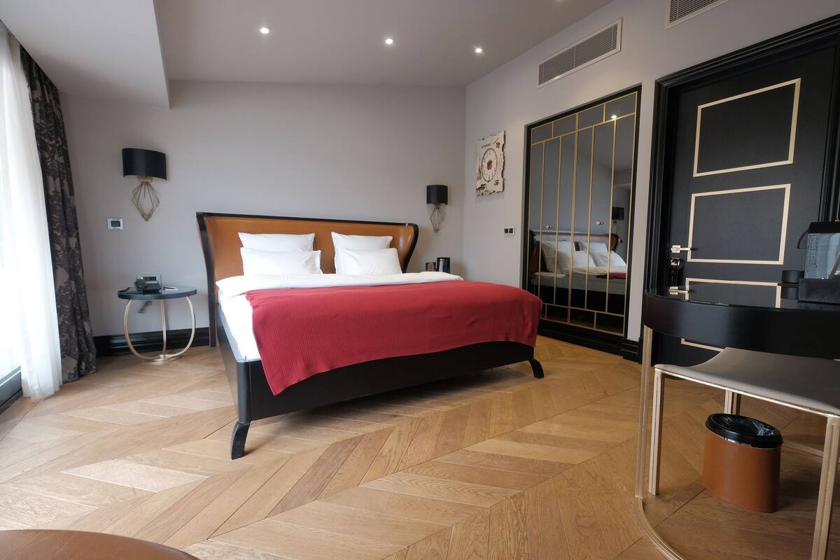 Una habitación de hotel moderna con una cama grande, un escritorio, un armario y un espejo.