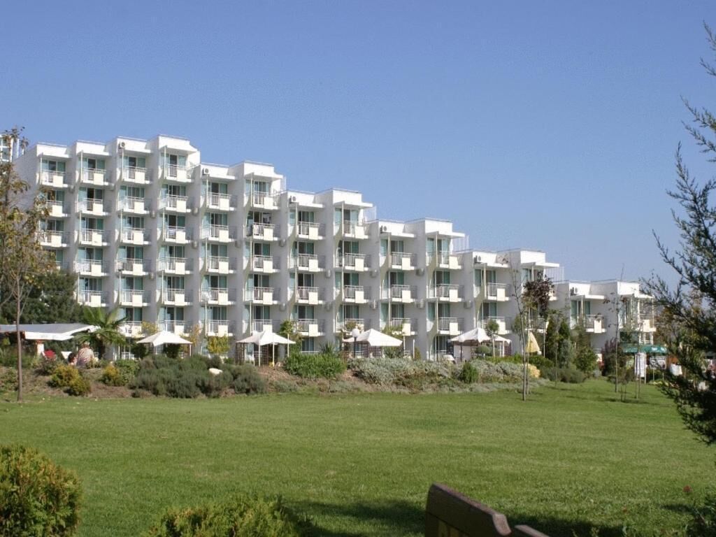 A multi-story hotel with balconies, a lawn in the foreground, and a clear sky.