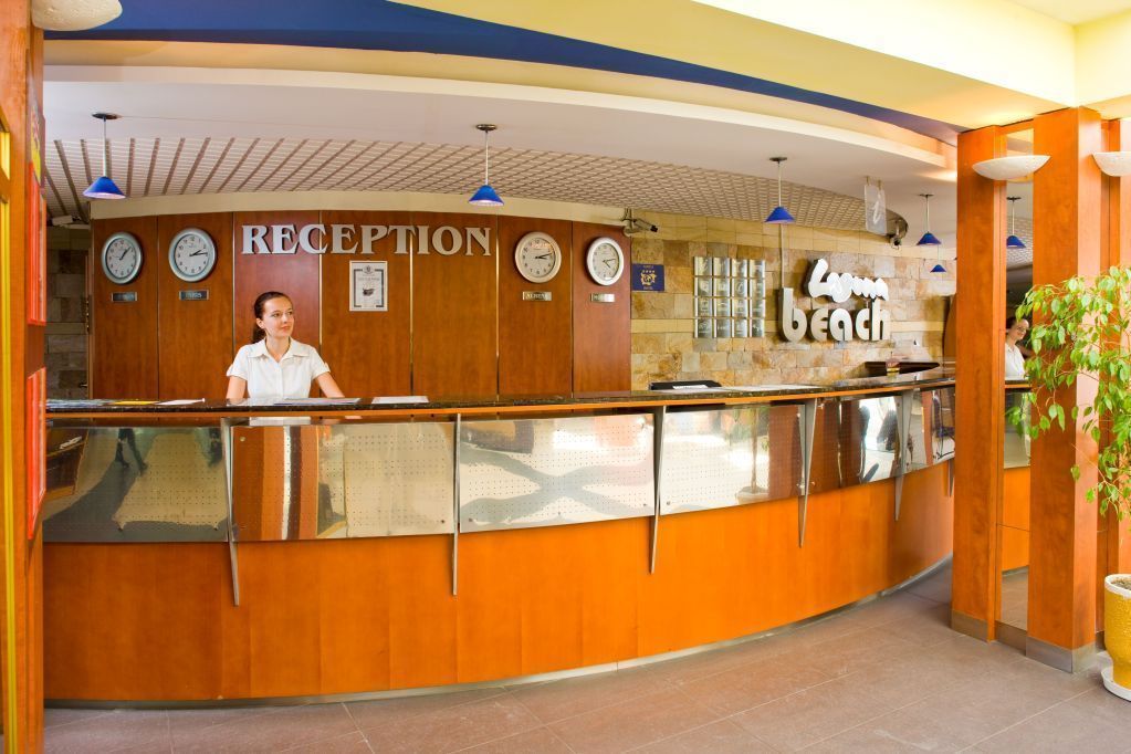 Un área de recepción con un mostrador de madera, relojes y un cartel que dice 'RECEPTION'.