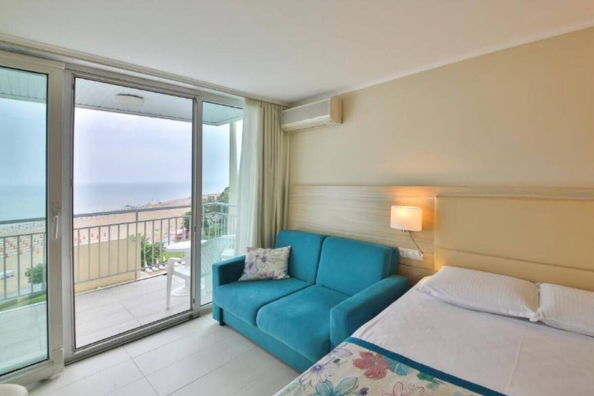 Una habitación de hotel con cama, sofá, balcón y vista, además de una lámpara de pared.