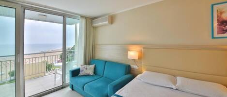 Una habitación de hotel con cama, sofá, balcón y vista, además de una lámpara de pared.