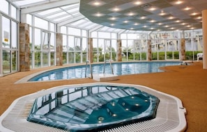 An indoor swimming pool with a hot tub, surrounded by large windows and a glass ceiling. - Hotel Laguna Beach (Albena)