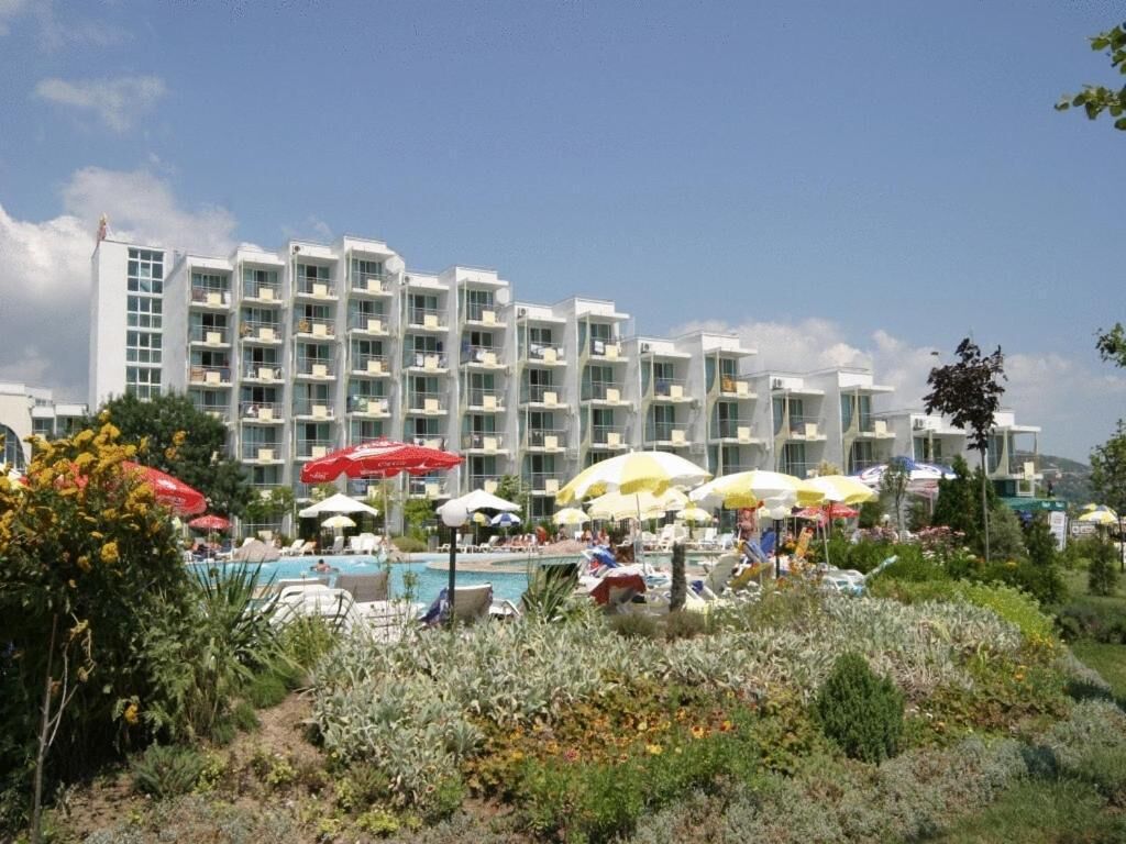 Un hotel con varios balcones, piscina y sombrillas para el exterior.