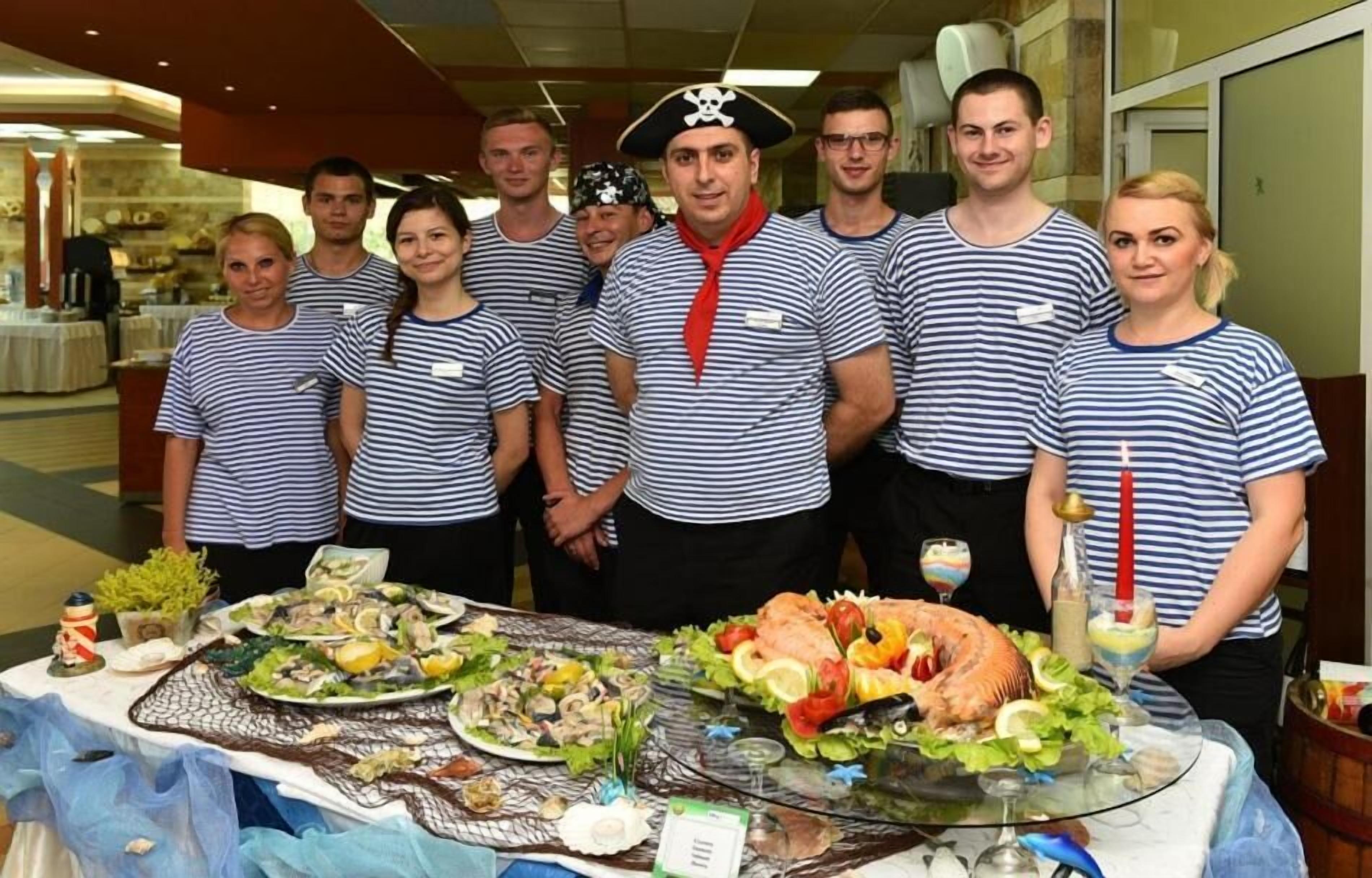 A group of people in striped shirts standing in a room with a table full of seafood dishes and drinks.