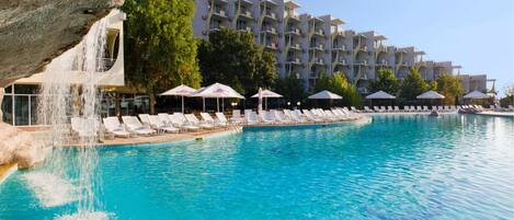 A hotel with a pool, lounge chairs, and umbrellas.