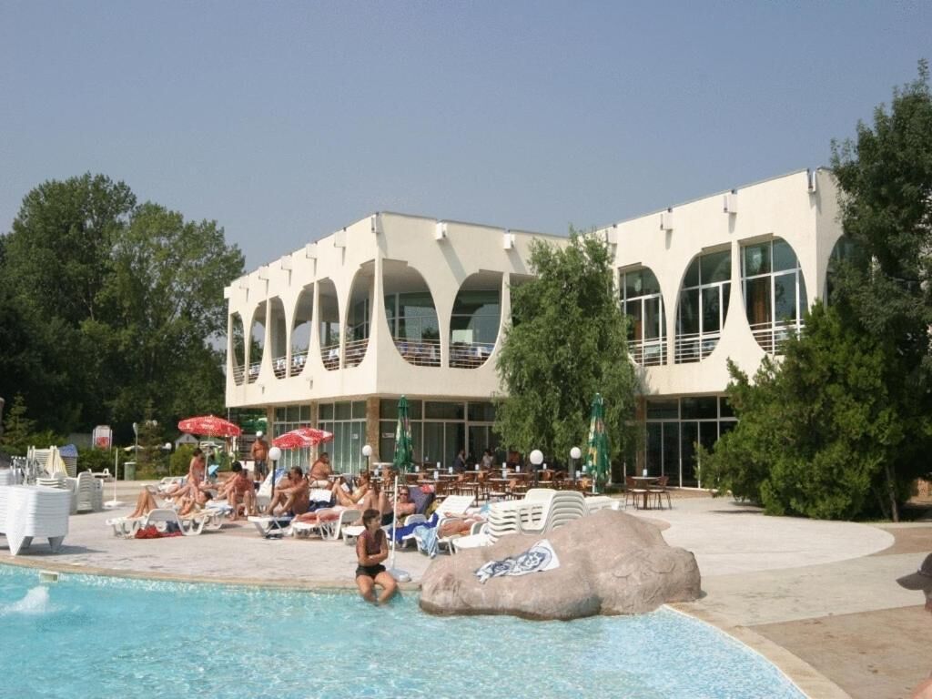 Ein Poolbereich mit Liegestühlen und Sonnenschirmen, ein großer Felsen mit Gestaltungselementen sowie ein Gebäude mit Rundbogenfenstern.