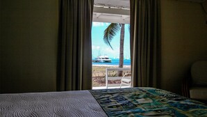 A hotel room with a bed, a view of the sea, and a palm tree. - Anegada Reef Hotel (Setting Point)